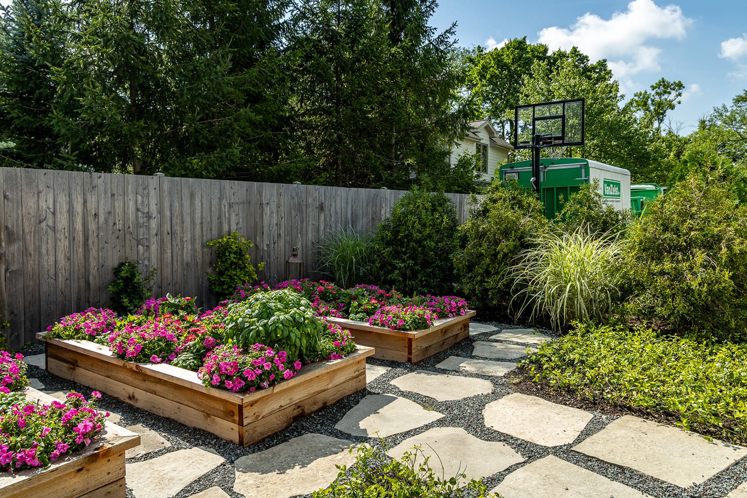 Raised wooden garden beds filled with flowering annuals and herbs beside a flagstone path in a private backyard landscape
