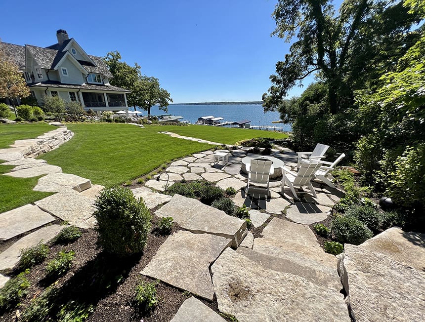 Completed lakeside fire pit with circular stone patio and Adirondack seating overlooking the lake in Williams Bay, Wisconsin.